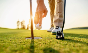 AdobeStock_313435180_Web Nahaufnahme Golfer steht am Loch auf gepflegtem Grün, bereit zum Einlochen.