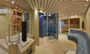 Wellnessbereich mit geschwungener Mosaikbank, Dusche mit blauen Fliesen, Holzdecke und mehreren Saunakabinen.
