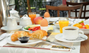 Frühstückstisch mit Croissant, gekochten Eiern im Eierbecher, Brotkorb, Marmelade, Butter, Orangensaft, Kaffee und frischem Obst