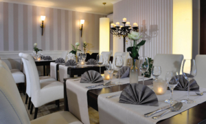 Elegant gedeckter Restauranttisch mit weißen Sesseln, gefalteten grauen Servietten, Kerzen und Blumenschmuck.