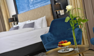 Doppelzimmer mit großem Bett, blauer Sessel, Beistelltisch mit Obst und einer weißen Rose in Vase.