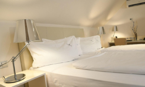 Hotelzimmer mit zwei weißen Einzelbetten unter einer Dachschräge, Nachttischen und modernen Lampen.