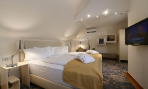Dachzimmer mit Doppelbett, heller Bettwäsche, Fernseher an der Wand und schräger Decke.