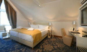 Hotelzimmer mit Doppelbett, gelbem Bettläufer, Sesseln und schräger Decke unter dem Dach.
