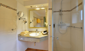 Helles Badezimmer mit Dusche, großem Spiegel, Waschbecken und Kosmetikspiegel.