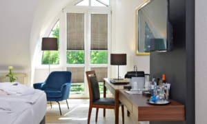 Doppelzimmer mit Sesselgruppe, Schreibtisch, Fernseher und rundem Fenster.