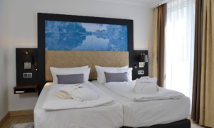 Doppelzimmer mit zwei Einzelbetten, gepolstertem Kopfteil und goldenen Vorhängen vor Fenster.