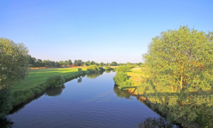 Celle_Winsen_Allerbruecke_Allerblick Flusslauf durch grüne Landschaft bei strahlend blauem Himmel.