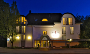 Hoteleingang bei Nacht mit beleuchtetem Vordach und heller Außenbeleuchtung.