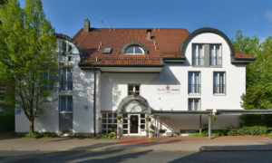 Hoteleingang mit weißer Fassade, rotem Dach und breiter Treppe bei Tageslicht.