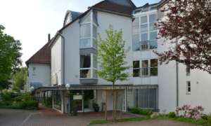 Zweiter Gebäudeflügel mit weißer Fassade, Balkon und kleinem gepflasterten Platz.