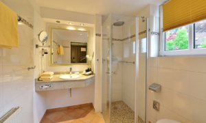 Badezimmer mit Waschbecken, Spiegel, Handtuchheizkörper und bodengleicher Dusche.