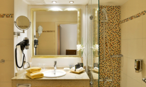 Badezimmer mit Dusche, großem Spiegel, Föhn, Kosmetikspiegel und Duschgelspender.