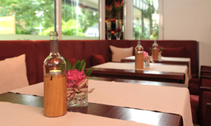 Hotel_Caroline_Mathilde_Celle_Restaurant_Bistro_Kanape_0511_093 Rote Polsterbank mit gedeckten Holztischen, Flasche und rosa Blume am Fenster.