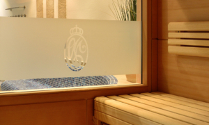 Hotel_Caroline_Mathilde_Celle_Sauna_Wellness_0023_3 Saunabereich mit Holzbank, Liegen, Glastür und dekorativem Kiesbett.