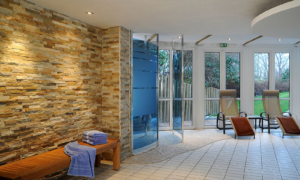 Hotel_Caroline_Mathilde_Celle_Schwimmbad_Pool_Wellness_0112_027 Ruhebereich mit Steinwand, Holzbank, Dusche und bodentiefen Fenstern.