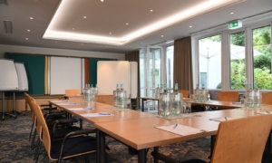 Seminarraum mit Wasserflaschen, Schreibunterlagen und Tageslicht durch große Fenster.