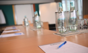 Konferenztisch mit Schreibunterlagen, Stift, Wasserflaschen und Gläsern.