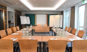 Konferenzraum mit U-förmig gestellten Tischen, Flipchart und Fensterfront.