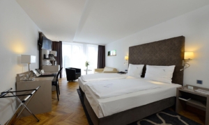 Doppelzimmer mit großem Bett, dunklem Kopfteil, Sesseln und bodentiefen Fenstern.