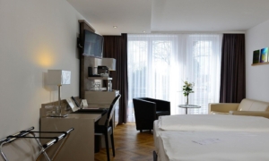 Zimmer mit Doppelbett, Schreibtisch, Fernseher, Kofferablage und Sitzbereich.