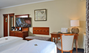 Doppelzimmer mit hellem Teppich, Spiegelkommode, Sitzbank und Schreibtisch mit Lampe.