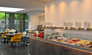 CM_Frühstück_0525_09 Buffetbereich mit Speisen, Geschirr und Blick in den modernen Frühstücksraum.