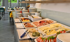 CM_Frühstück_0525_14 Buffet mit Wurst, Käse, Gemüse, Brot, Tellern und Frühstückszubehör.